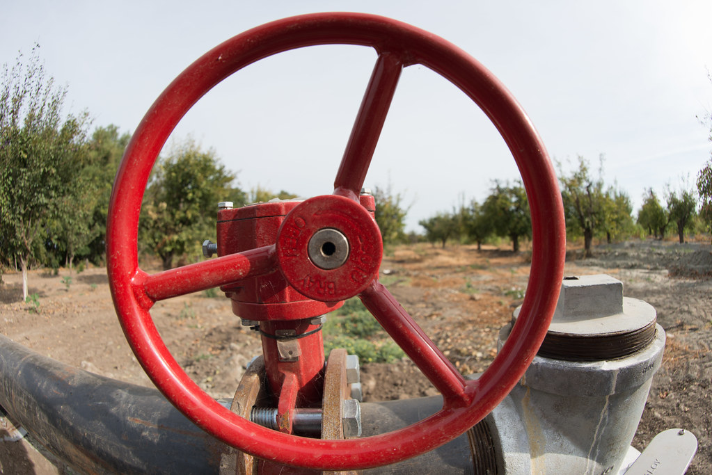 Roue de vanne d'irrigation rouge dans un verger, illustrant les raccords et pièces d'irrigation sur mesure