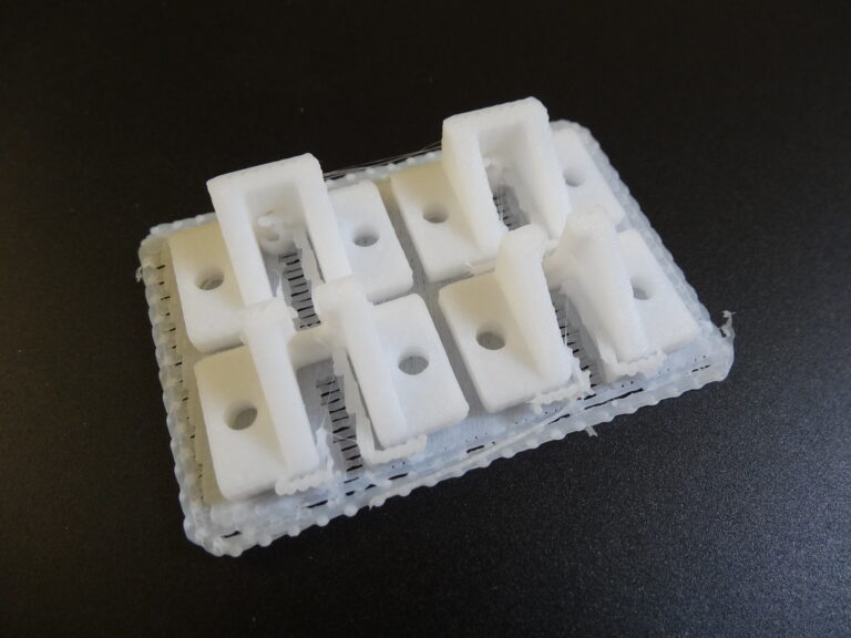 Plusieurs petites pièces de fixation blanches fraîchement imprimées en 3D, illustrant des angles et congés sur des pièces mécaniques