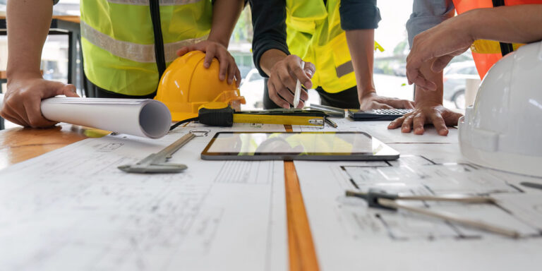 Plans techniques déroulés sur une table avec un pied à coulisse et une tablette, illustrant la préparation d'un fichier technique