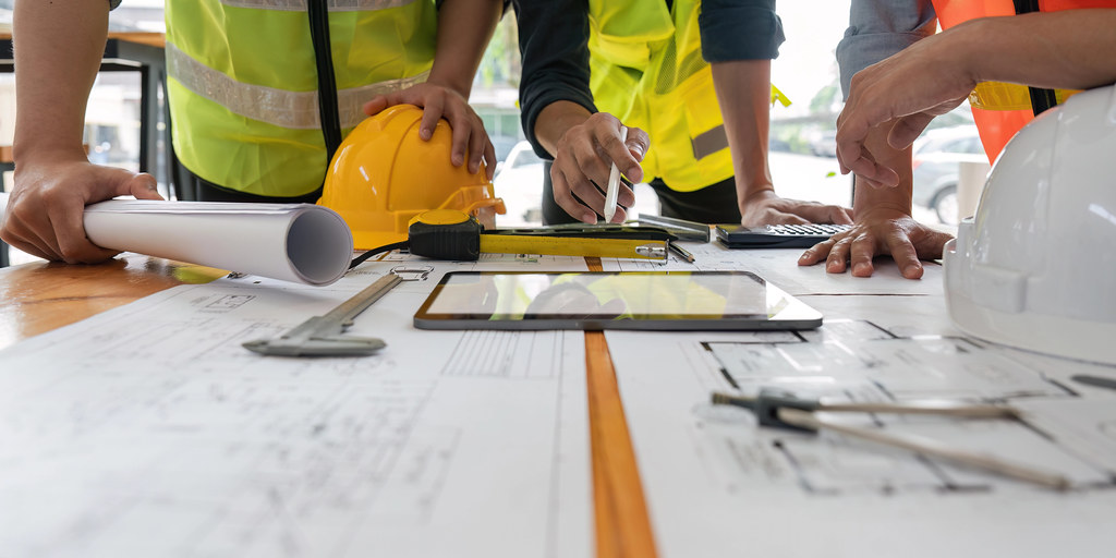 Plans techniques déroulés sur une table avec un pied à coulisse et une tablette, illustrant la préparation d'un fichier technique