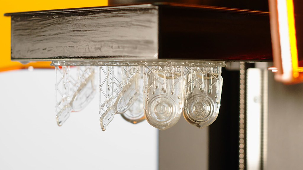 Pièces transparentes fraîchement imprimées en résine, encore attachées à leurs supports sur le plateau d'une imprimante SLA