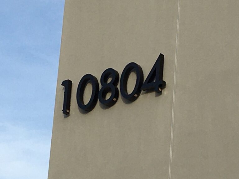 Numéro d'adresse en chiffres noirs en relief fixés sur une façade de bâtiment, illustrant la signalétique extérieure permanente